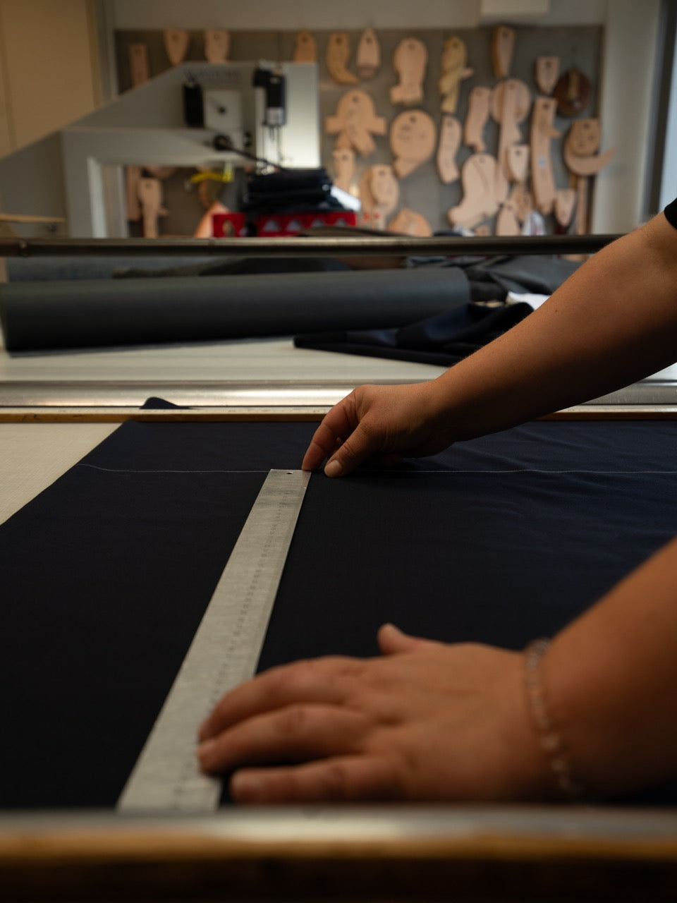 Hand mit Lineal markiert dunklen Wollstoff vor Schnittmustern an der Wand